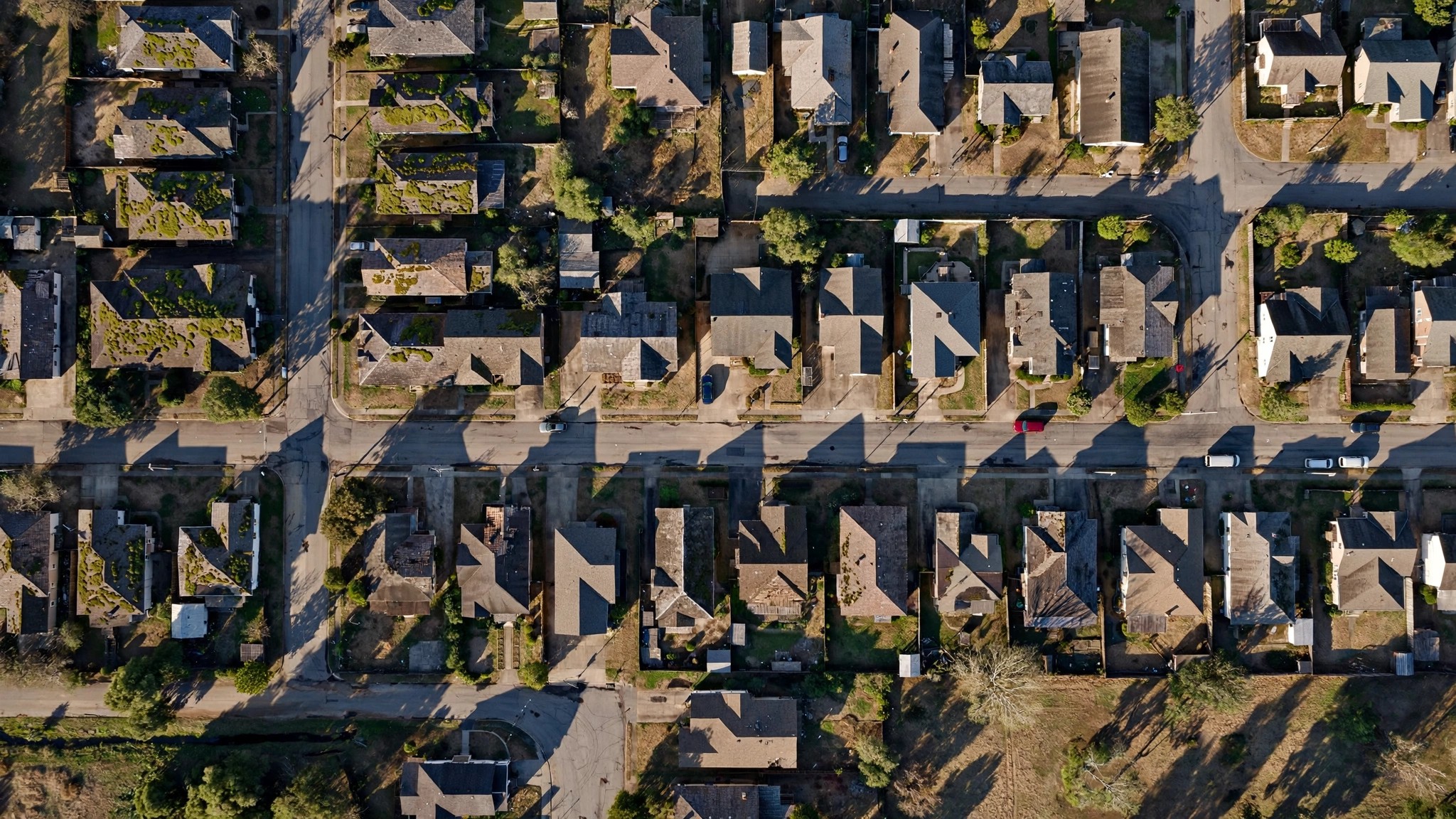 Aerial satellite view of suburban residential rooftops with subtle digital scoring overlays and color-coded condition markers