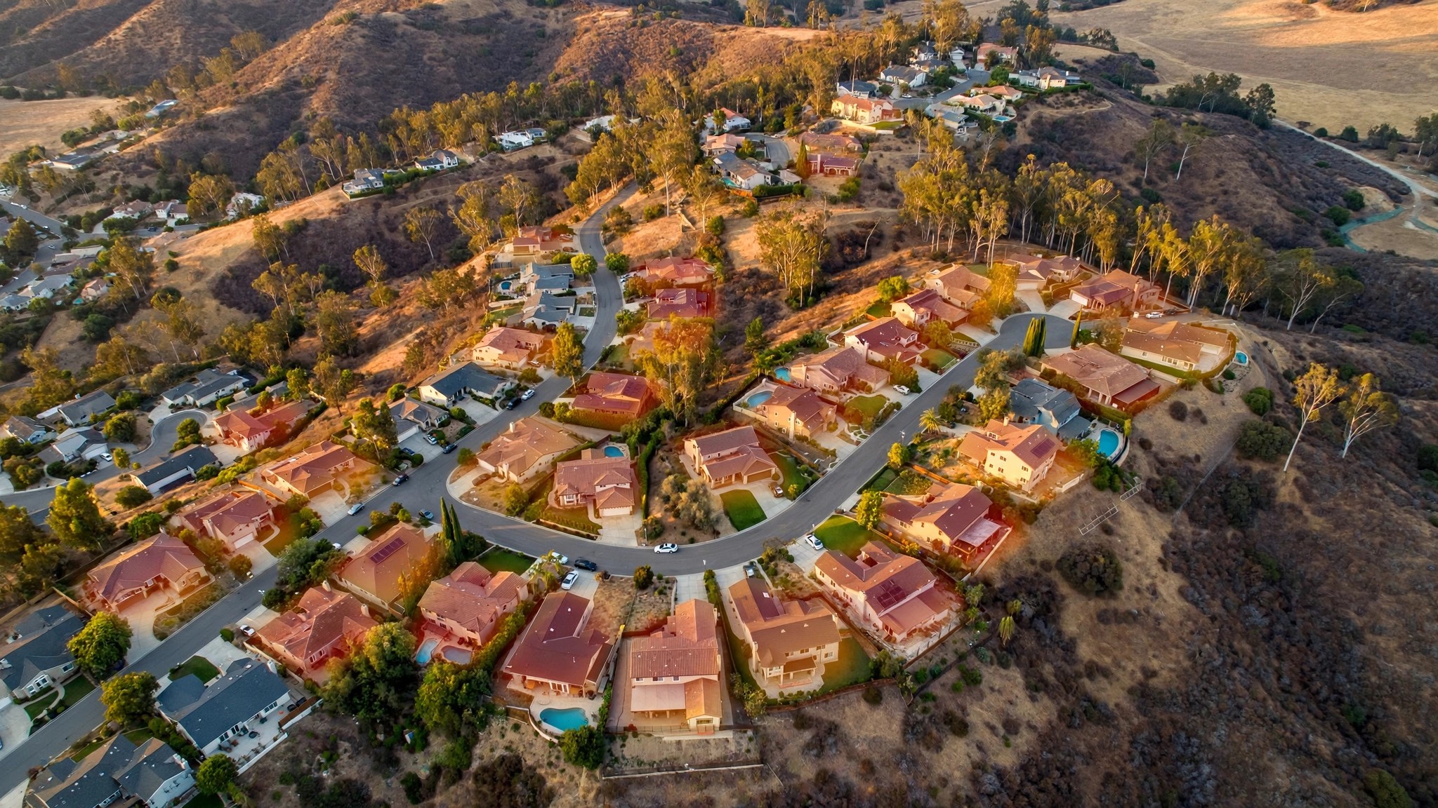 An aerial view of California hillside homes bordered by dry brush, with faint digital scoring overlays on individual properties