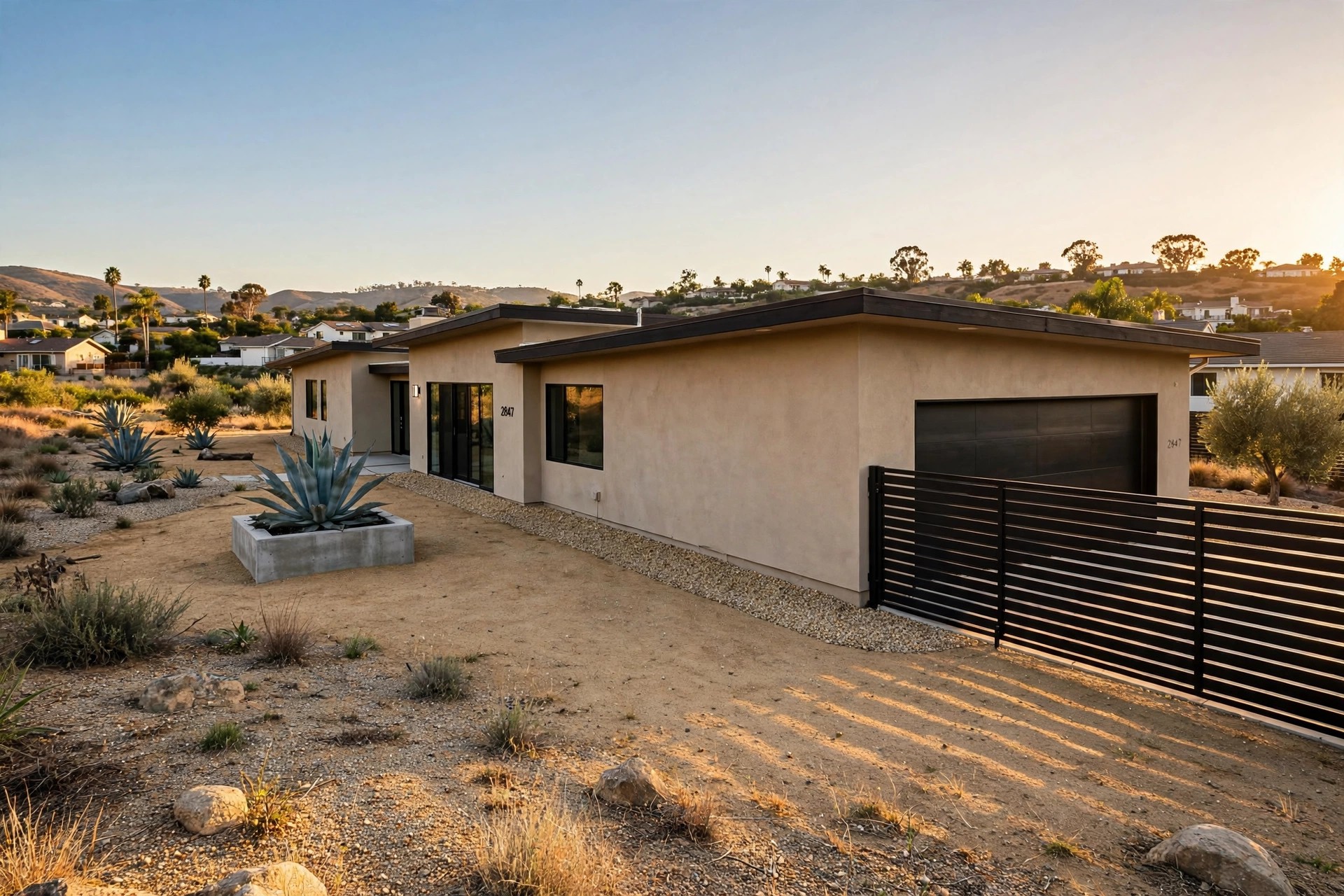 California home with a five-foot band of gravel and decomposed granite around its foundation, steel fence panel where the fence meets the garage, warm late-afternoon light